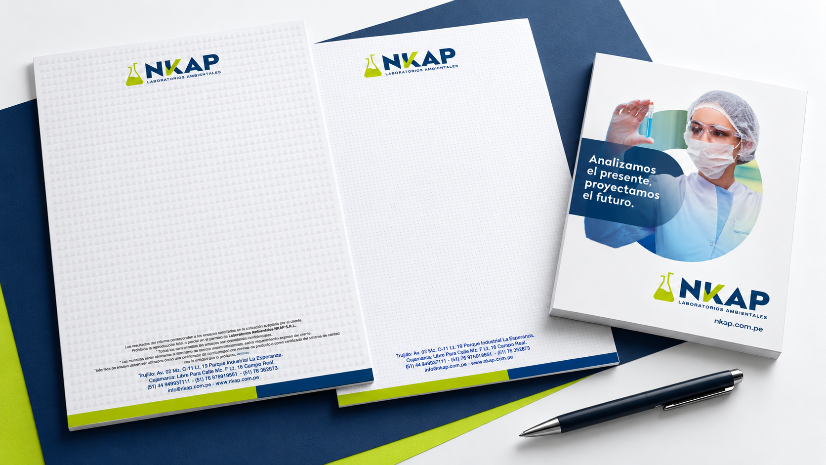 Papelería de NKAP Laboratorios Ambientales con hojas membretadas, un folleto institucional y un bolígrafo sobre fondos azul y verde